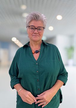 Eine ältere Dame mit grüner Bluse und einer Brille auf den Augen.