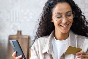 Frau hält Smartphone und Prepaid-Karte – Online-Bezahlung, geeignet für Gutscheine und Onlinedienste.