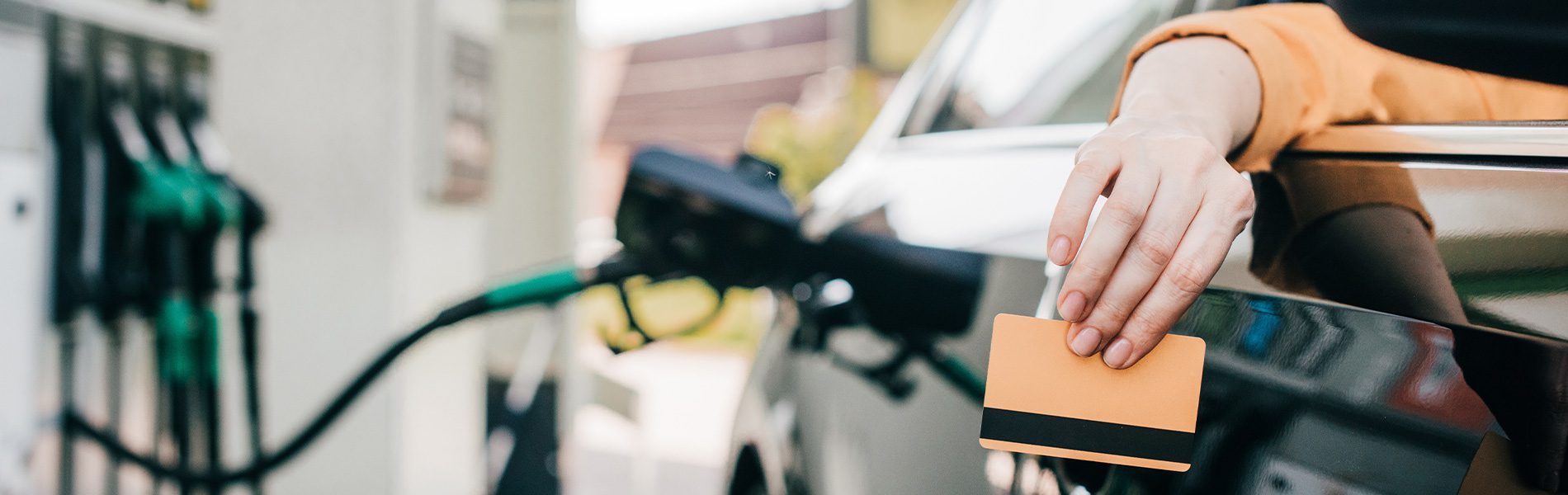 Hand mit EC-Karte am Auto vor Zapfsäulen – Flotten-/Tankkarte.