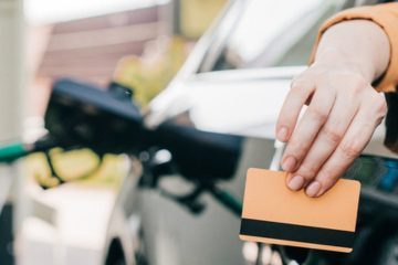 Hand mit EC-Karte am Auto vor Zapfsäulen – Flotten-/Tankkarte.